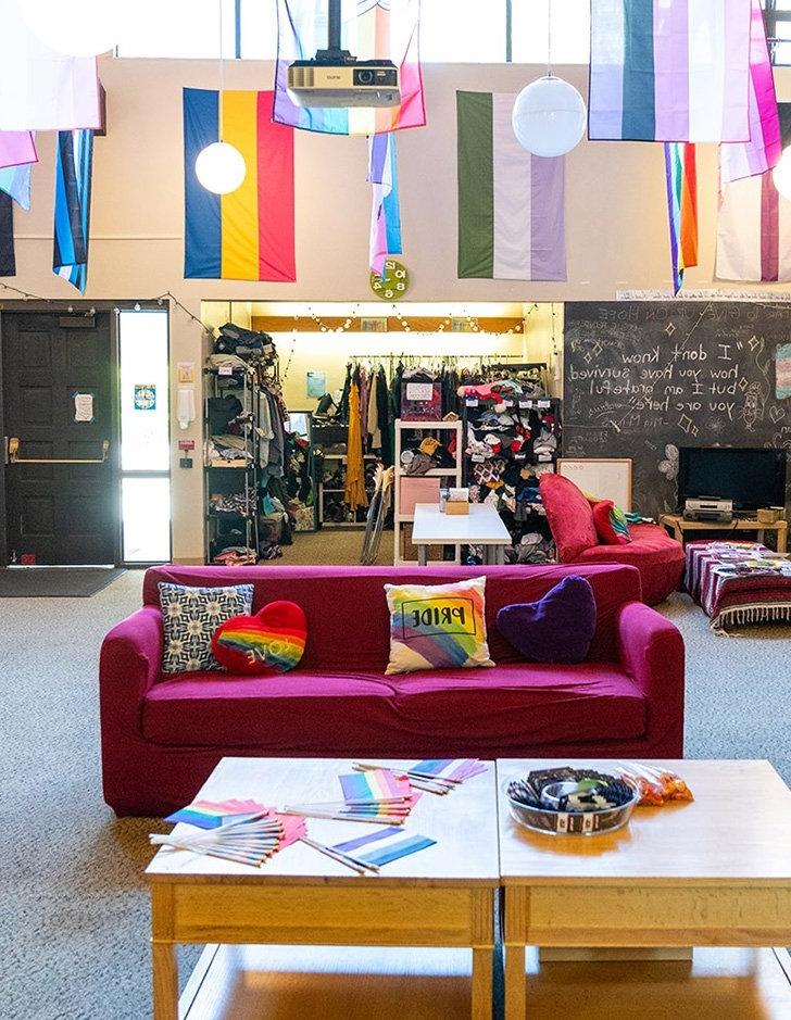 the colorful queer resource center living room with a pink couch and various lgbtqia flags on the walls